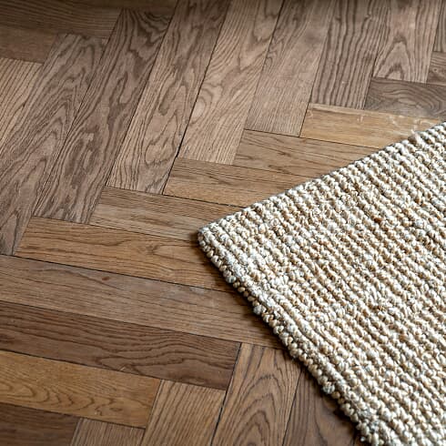 Herringbone hardwood floor with the corner of a woven rug