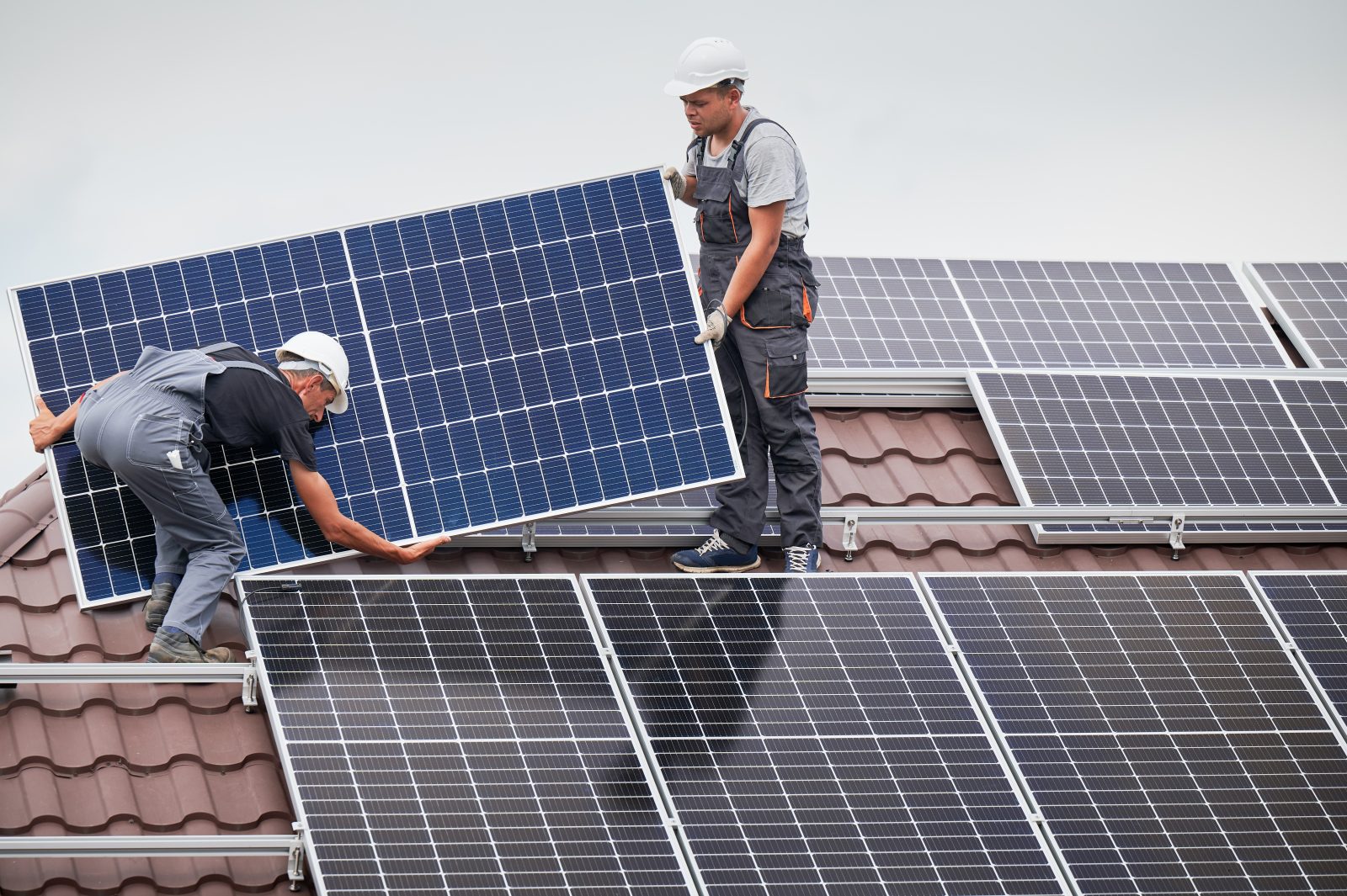 Two installers fitting solar panels on a tile roof