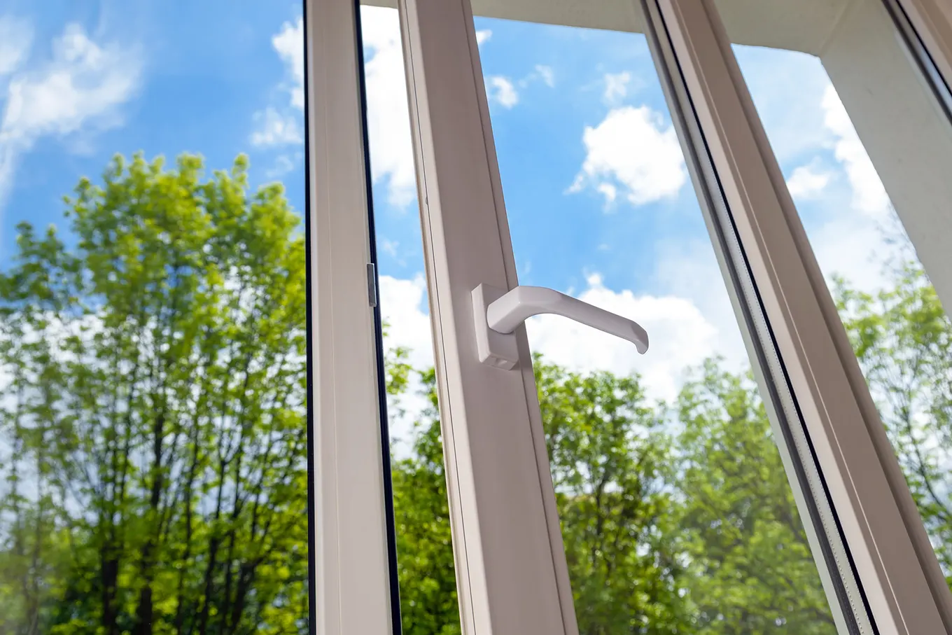 Open white casement window looking out onto trees and a blue sky