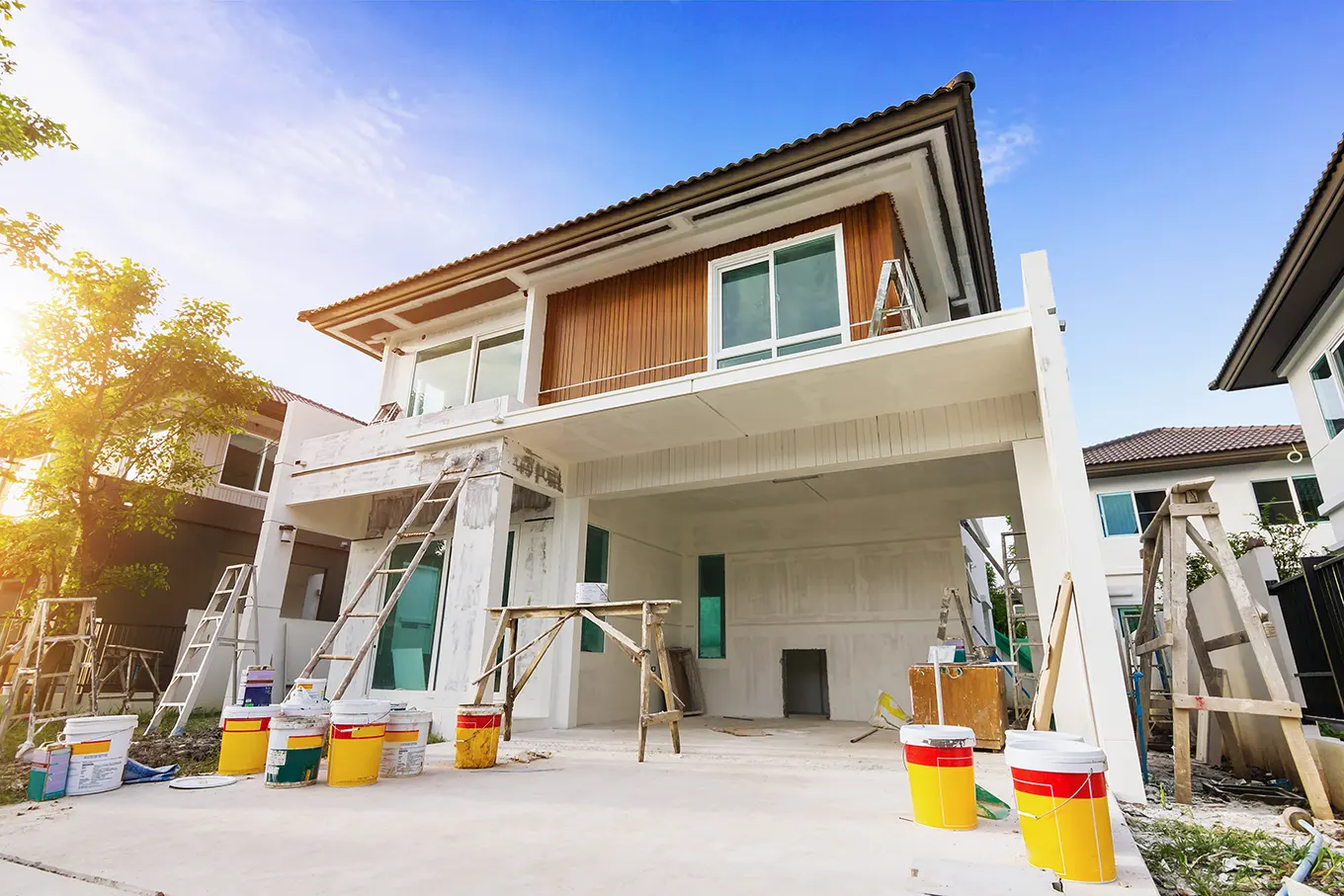 Two-storey house exterior being painted, with ladders and paint buckets in the driveway